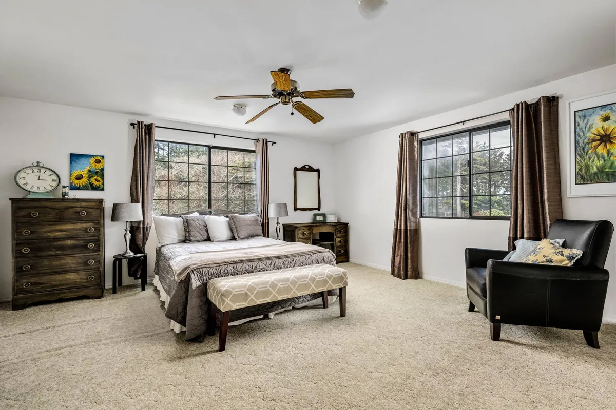 A tranquil and cozy bedroom featuring a queen bed, dresser, armchair, large windows that let in abundant morning light, and a decorative painting that adds warmth and charm. The soft lighting and relaxed atmosphere create a peaceful space for rest and solitude.