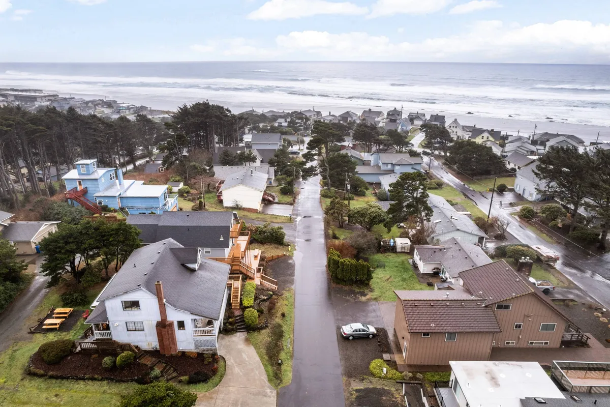 A tranquil view capturing the ocean, neighborhood houses, and a lush tree line. The scene is imbued with natural light and evokes the proximity to the beach and local walking paths.