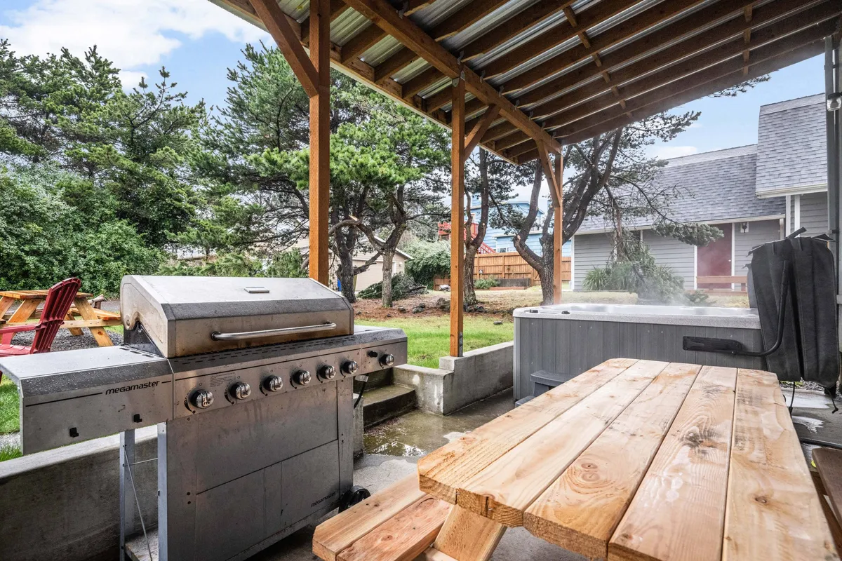 A welcoming backyard setup with a grill, hot tub, wooden table, and landscaped surroundings. The space invites barbecuing, soaking in the hot tub, and evening relaxation under the stars.