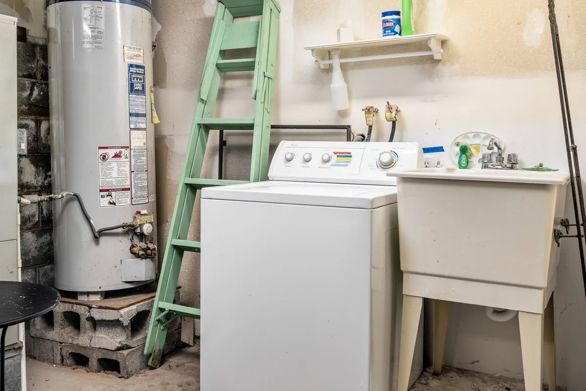A functional laundry area with a washing machine, utility sink, green ladder, and water heater, set up for practical use. The arrangement makes it clear that longer stays are comfortable and chores are simplified.