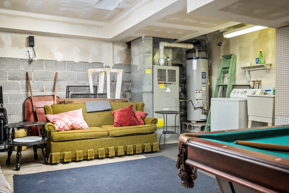 This image reveals a garage space featuring a green couch with pillows, a pool table, and a visible washing machine and water heater in the background. The informal and multi-use nature of the garage is showcased, highlighting both recreational and laundry functions.