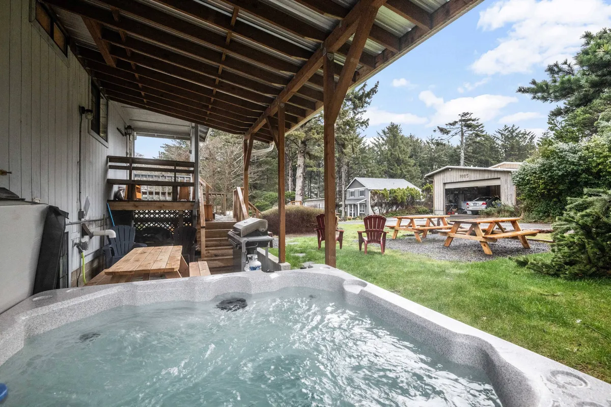 A cozy outdoor area with a bubbling private hot tub surrounded by lush greenery and a picnic table nearby. The space exudes relaxation, with the hot tub positioned for enjoying peaceful or social evenings under the stars.